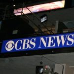 The CBS News sign displayed inside a television news studio with broadcasting equipment visible overhead.