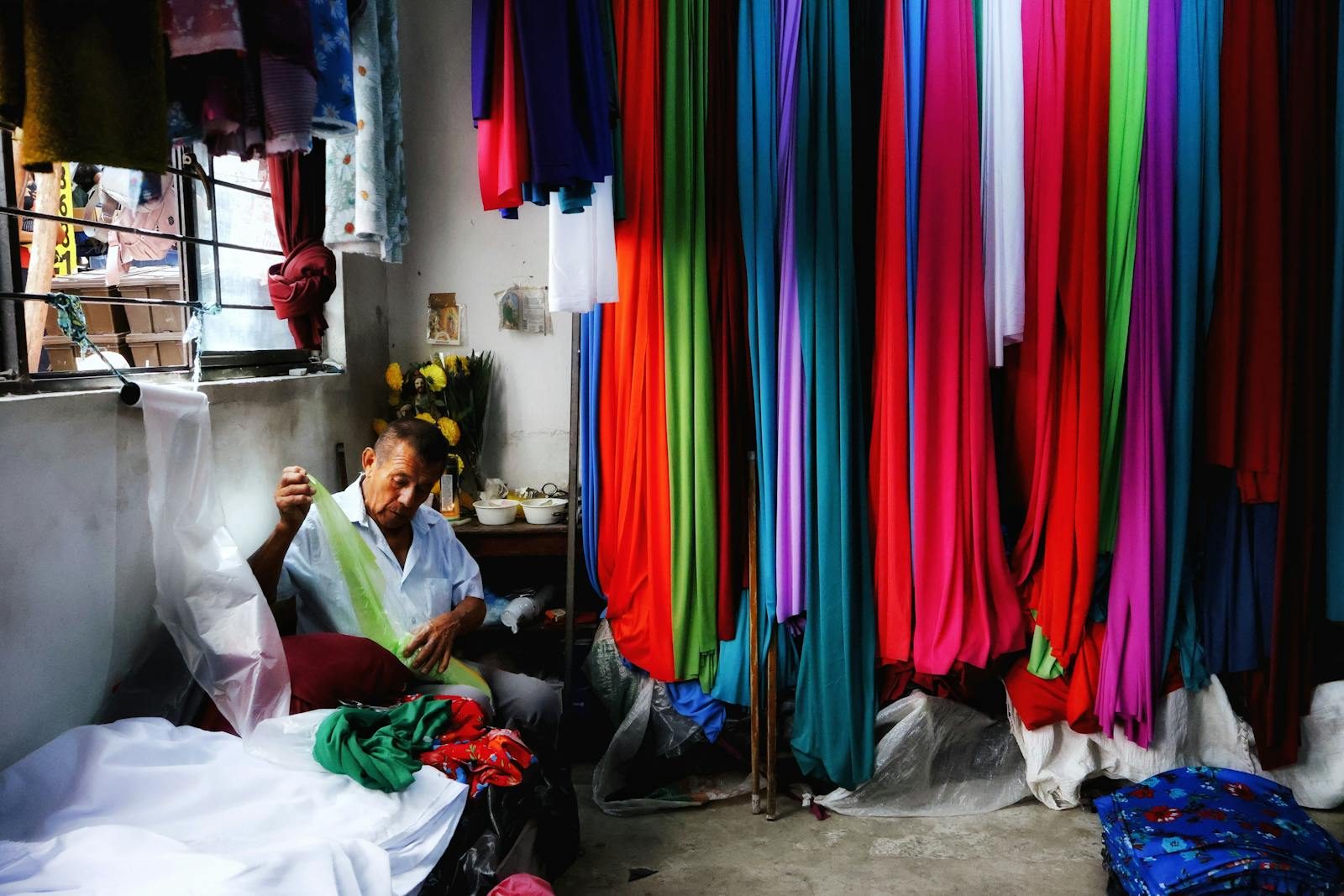 A tailor working with diverse textiles in a vibrant fabric shop, surrounded by colorful materials.