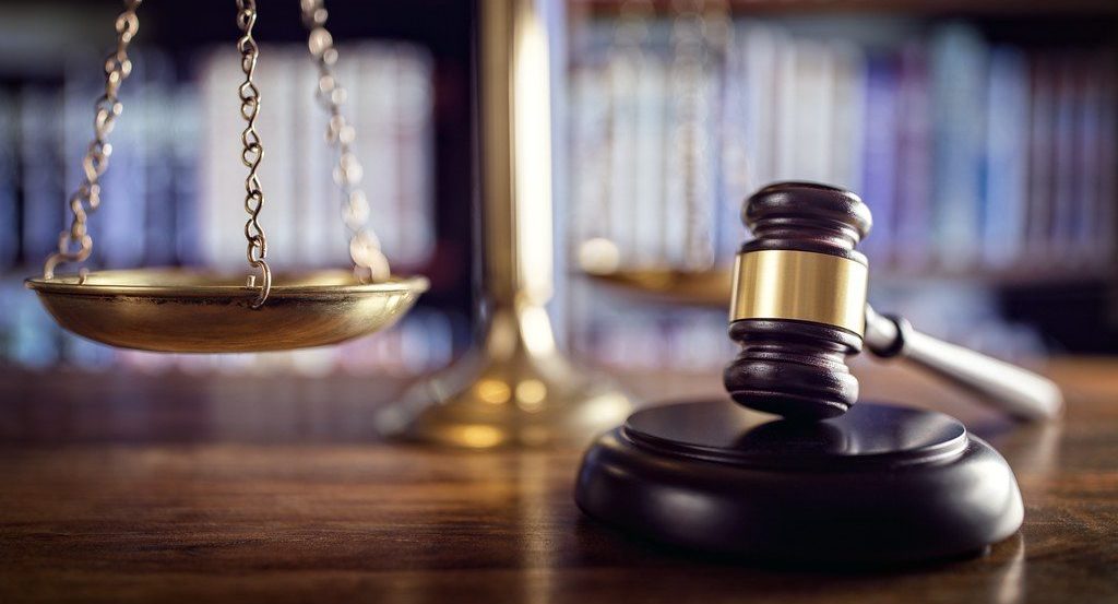 A wooden gavel resting on a sound block beside a golden scales of justice on a wooden surface.