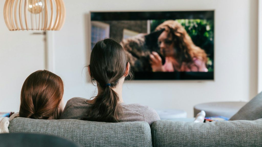 A couple of women sitting on a couch while watching TV.