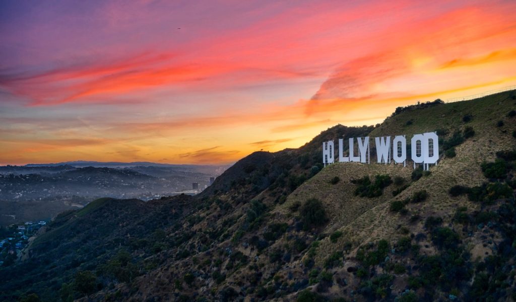 The iconic Hollywood sign glows against a vibrant sunset sky over the hills of Los Angeles.