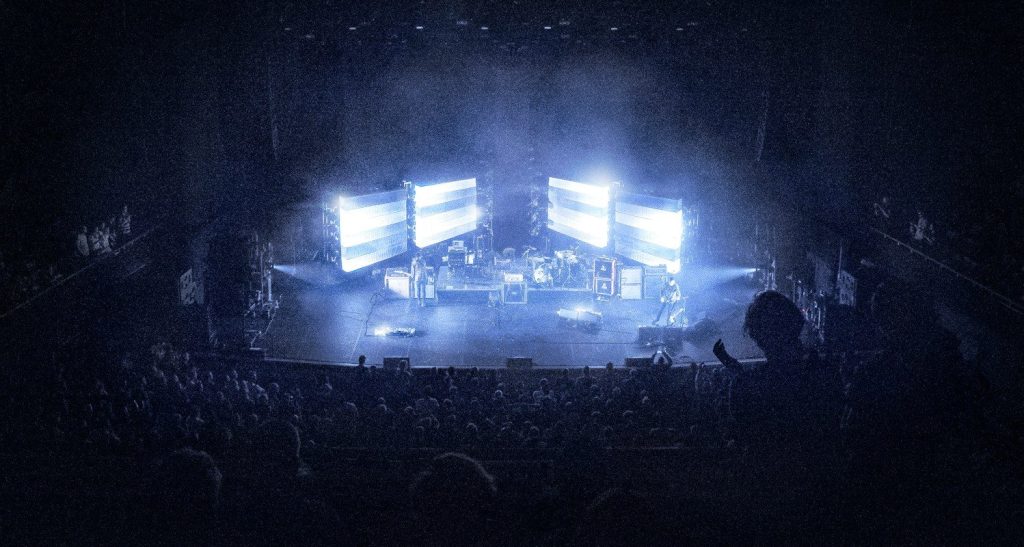 A wide view of a brightly lit live performance stage with large screens and a packed audience during a television event.
