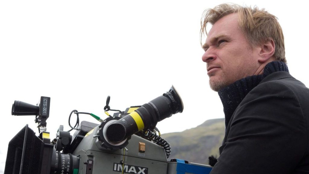Christopher Nolan holding an IMAX camera on an outdoor film set.