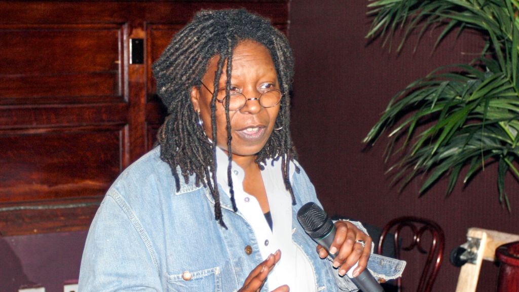 Whoopi Goldberg at an event holding a microphone.