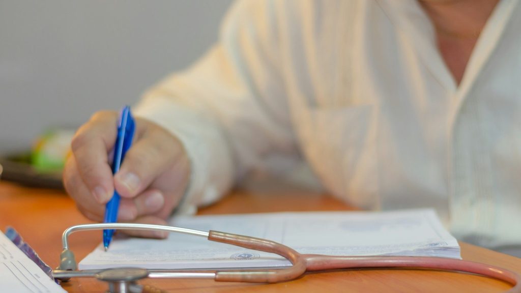 A person writing on a piece of paper with a stethoscope.