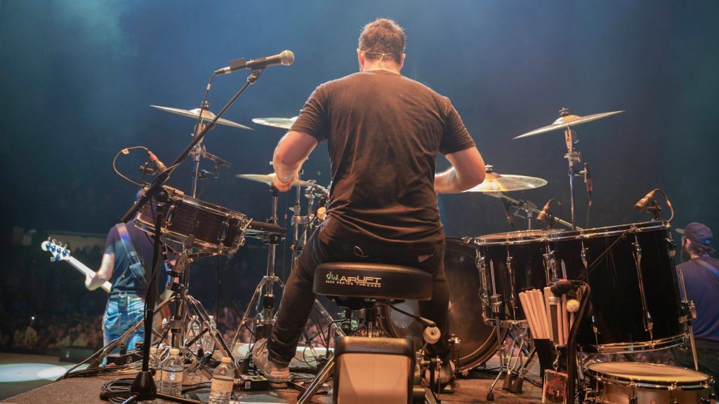 A back view of a man playing a drum set.
