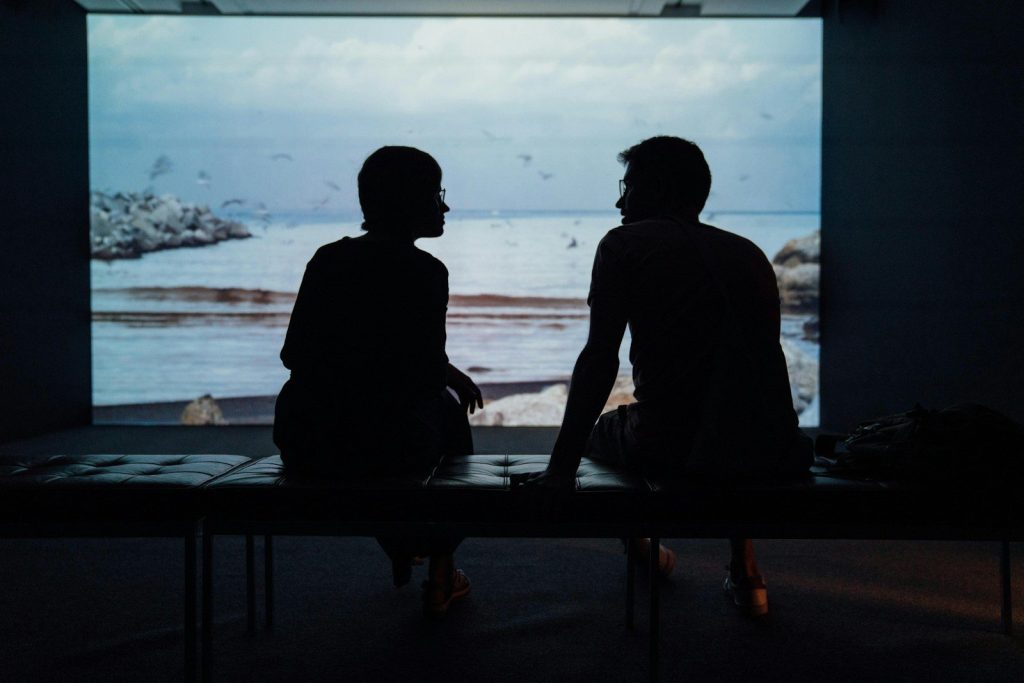Silhouette of a man and a woman sitting on an ottoman.