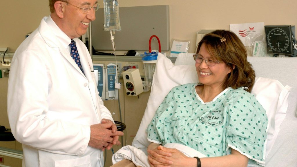 Doctor speaking with a smiling patient sitting in a hospital bed during a medical checkup.