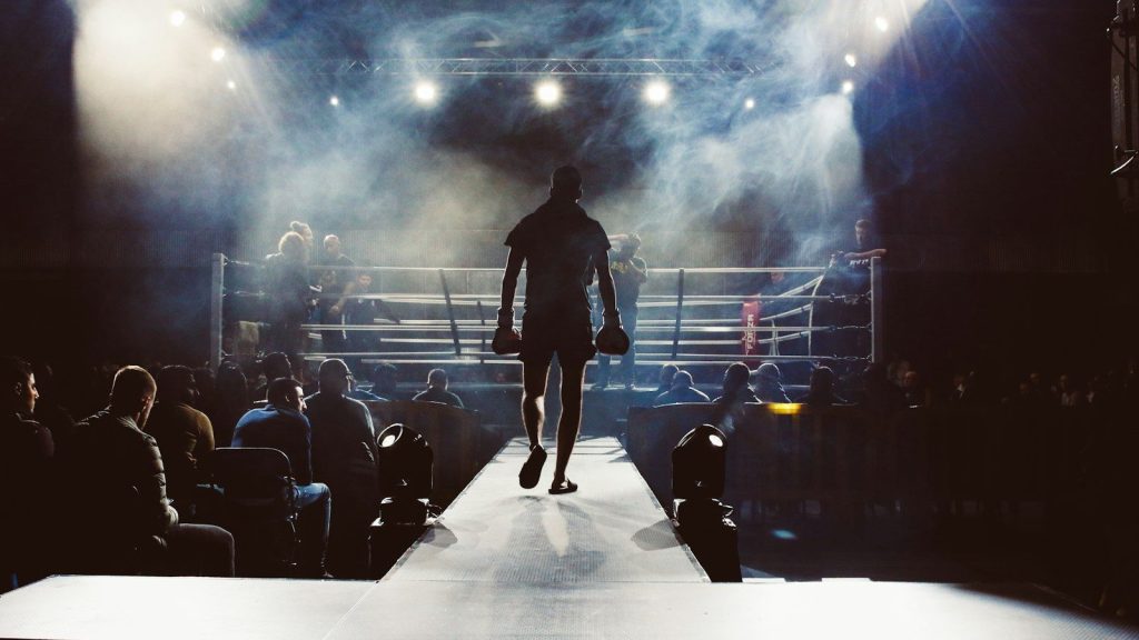 A boxer walking in a boxing ring surrounded by people.
