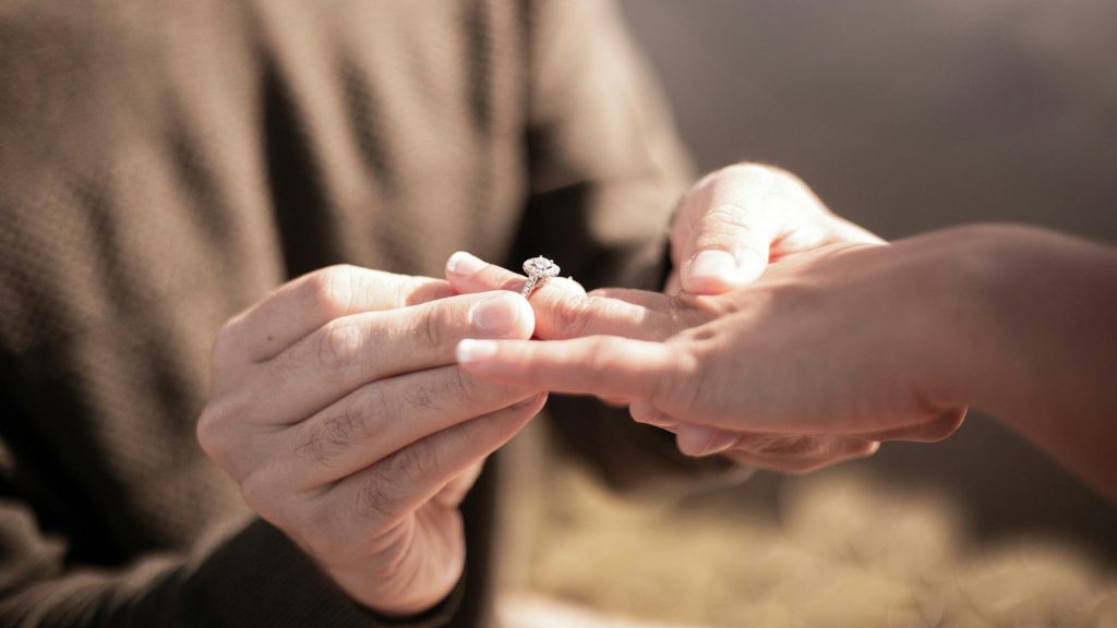Man placing a diamond engagement ring on a woman's finger.