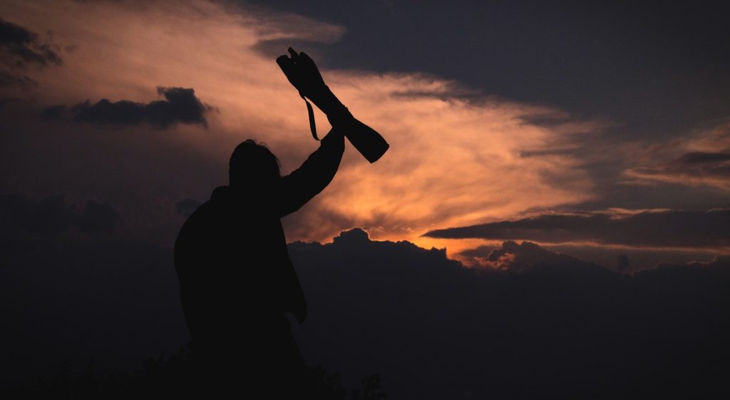 Silhouette of a person under cloudy skies raising a trophy.