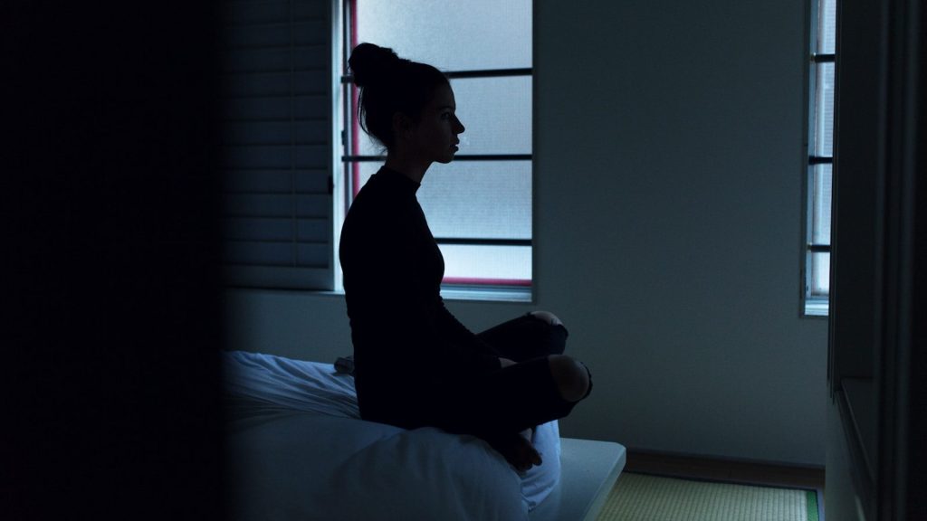 Woman sitting on a bed in a dark room.