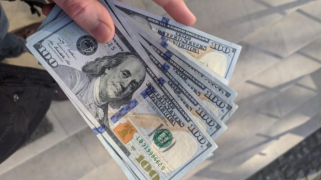 A person holding 100 U.S dollar bills.