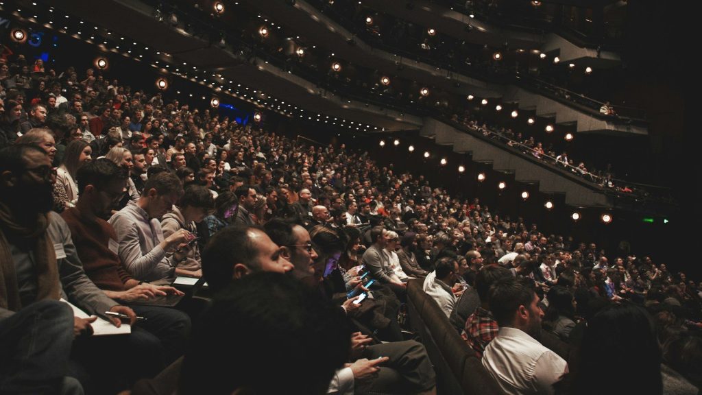 A large audience gathers inside a modern theater during a live event.