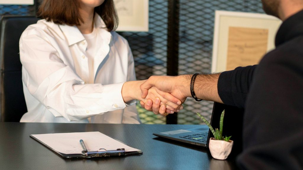 A man and a woman shaking hands in front of a laptop.