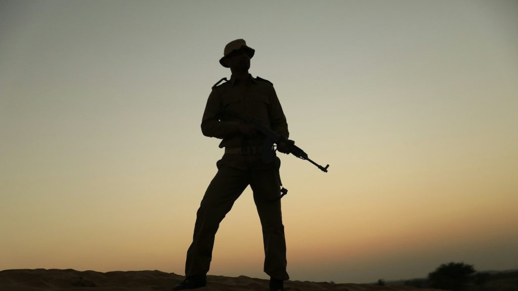 A silhouette of a soldier holding a rifle in the desert.