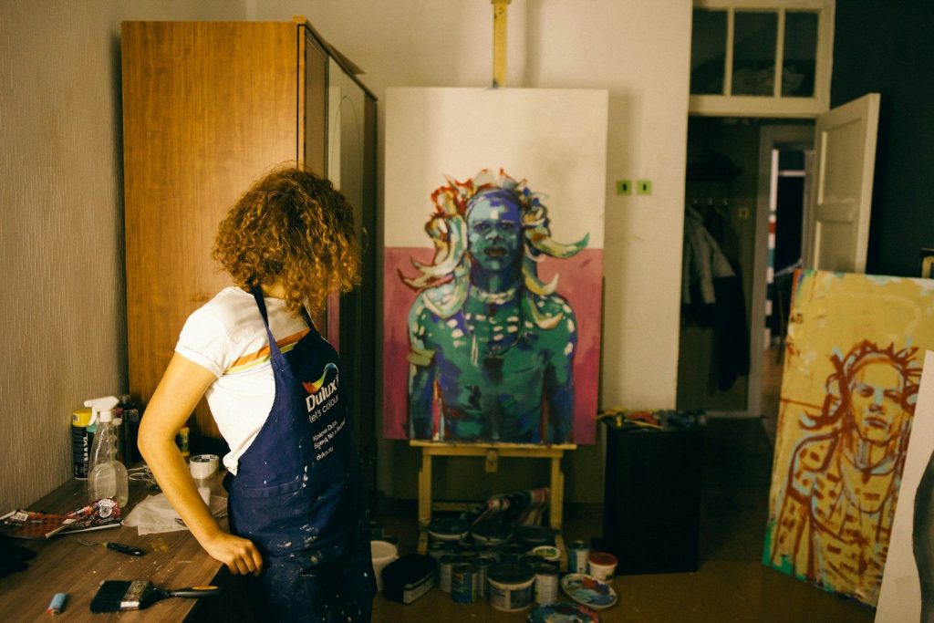 A woman standing by the support of a table watching her paintings.
