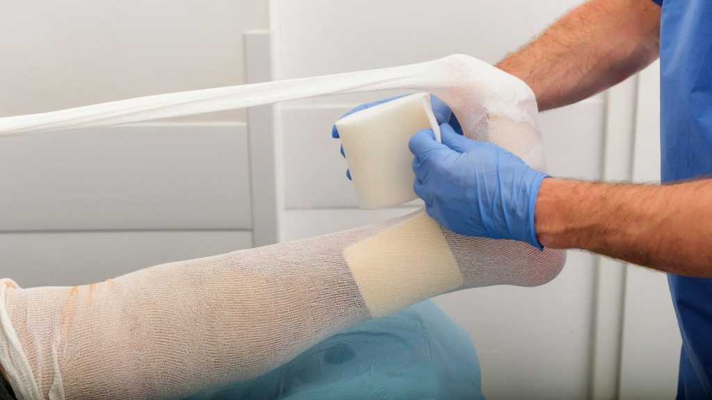 A man putting a medical bandage on the foot of a person.