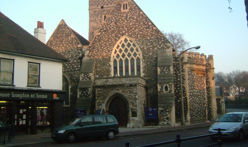 A historic stone church stands beside a street with parked cars.