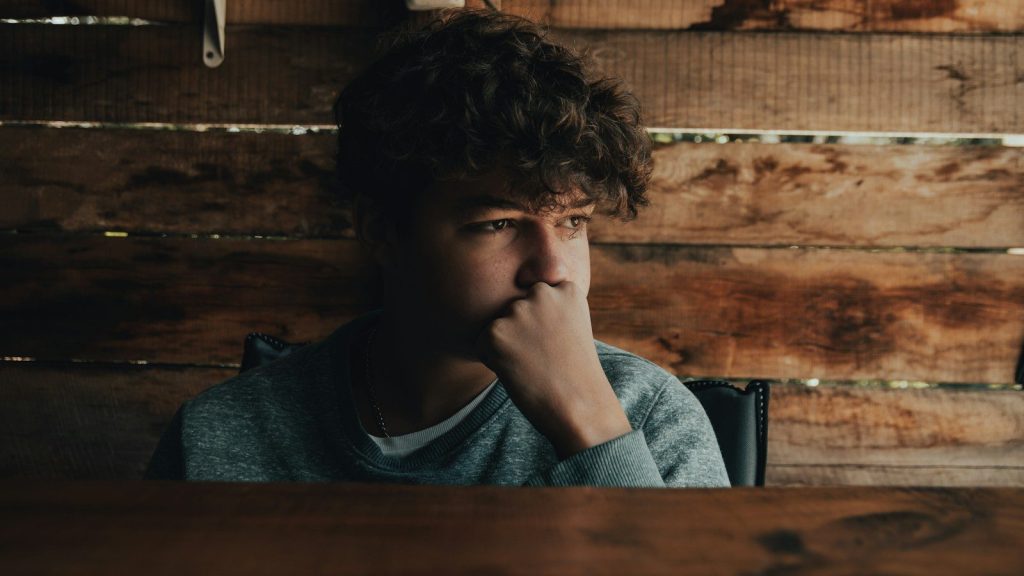 A boy sitting in front of a wooden wall.