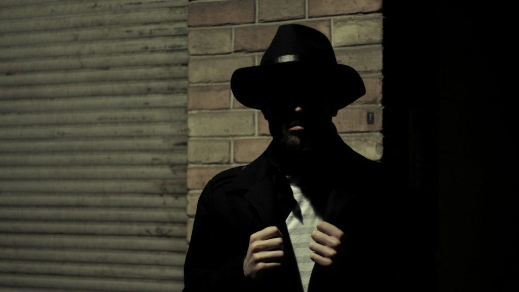 Silhouette of a man wearing a black fedora hat and a black suit jacket.
