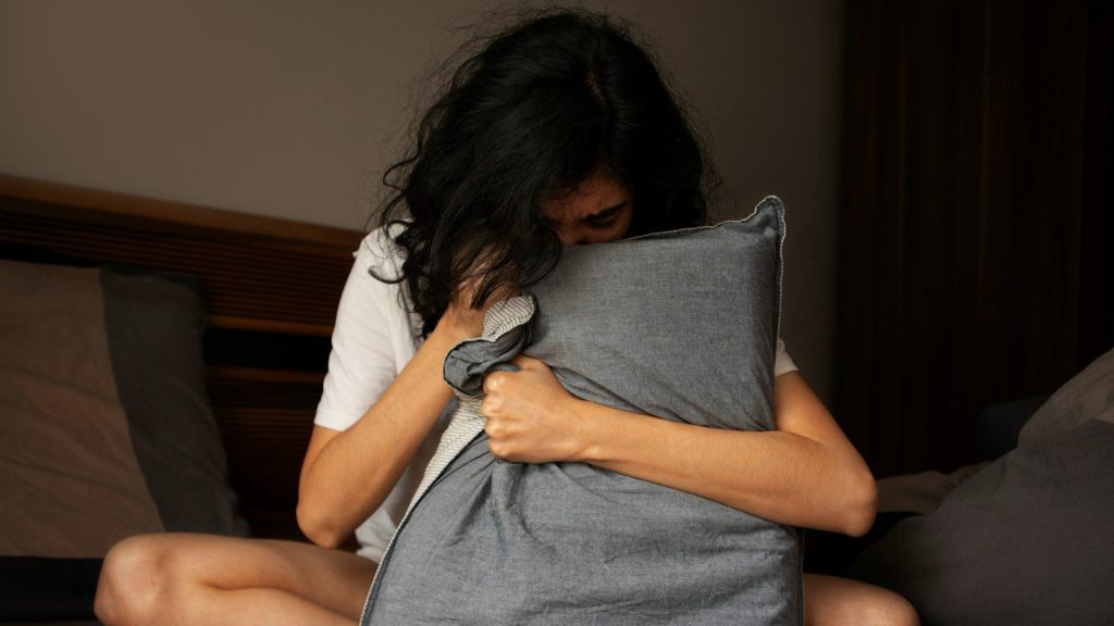 A woman sitting on a bed holding a pillow.
