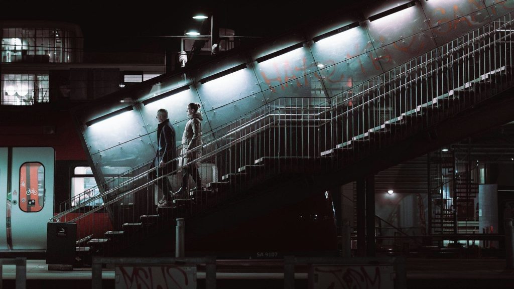 Two people walk up illuminated stairs at night.