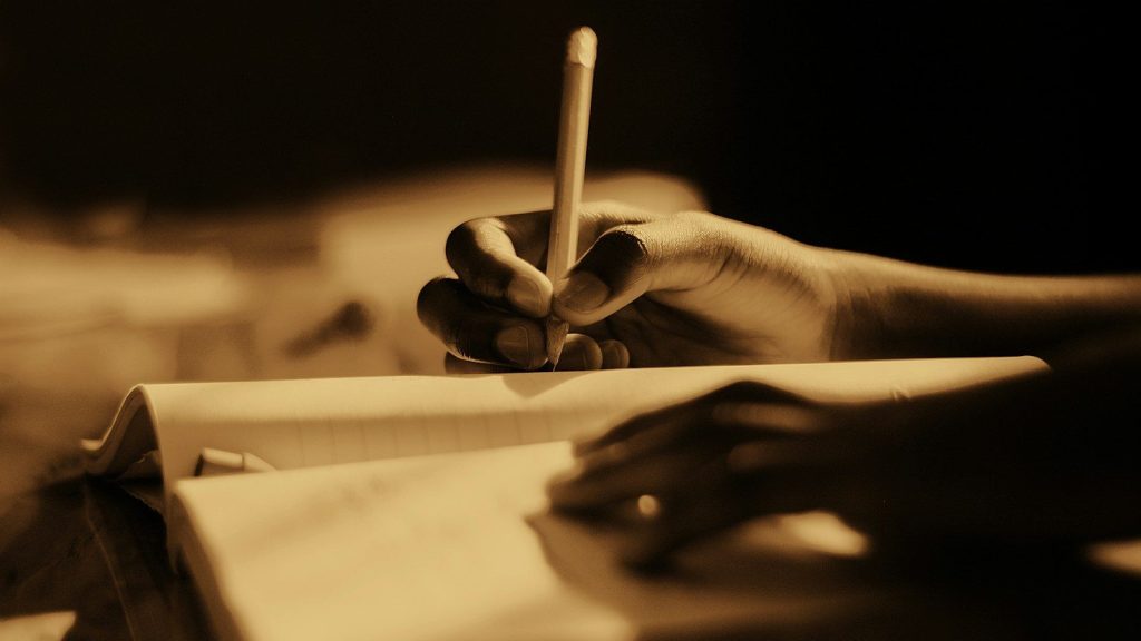a person holding a pen and writing on a book.