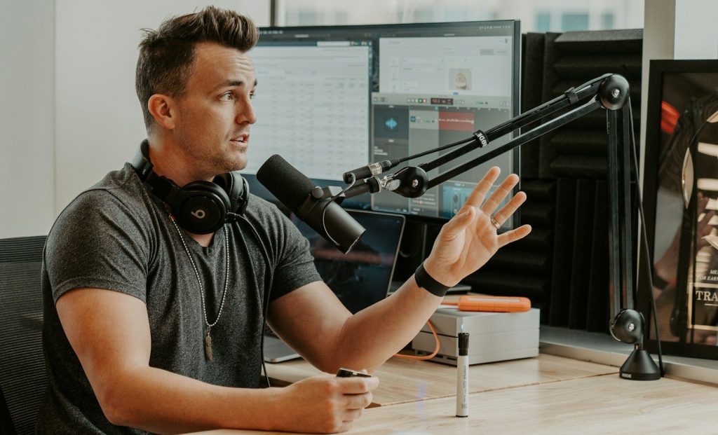 Man wearing grey shirt sitting by the table using microphone.
