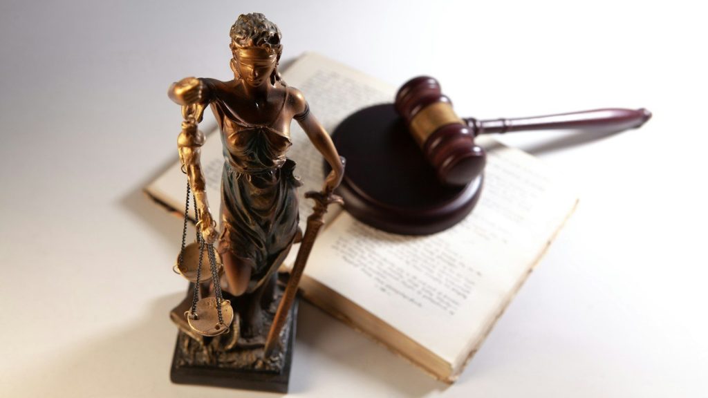 Statue of justice, gavel, and open book on table.