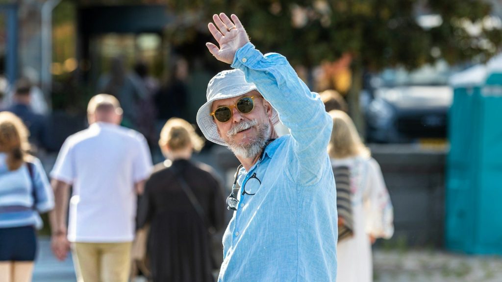 A man in a hat and sunglasses waving.