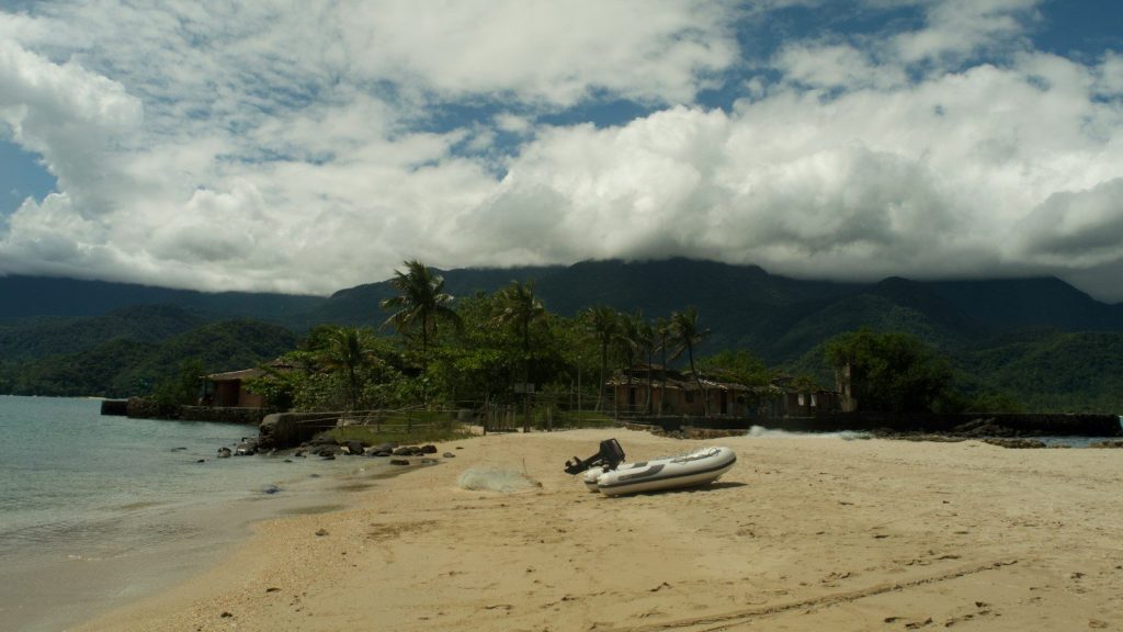 Small boat on a sandy beach with mountains behind.