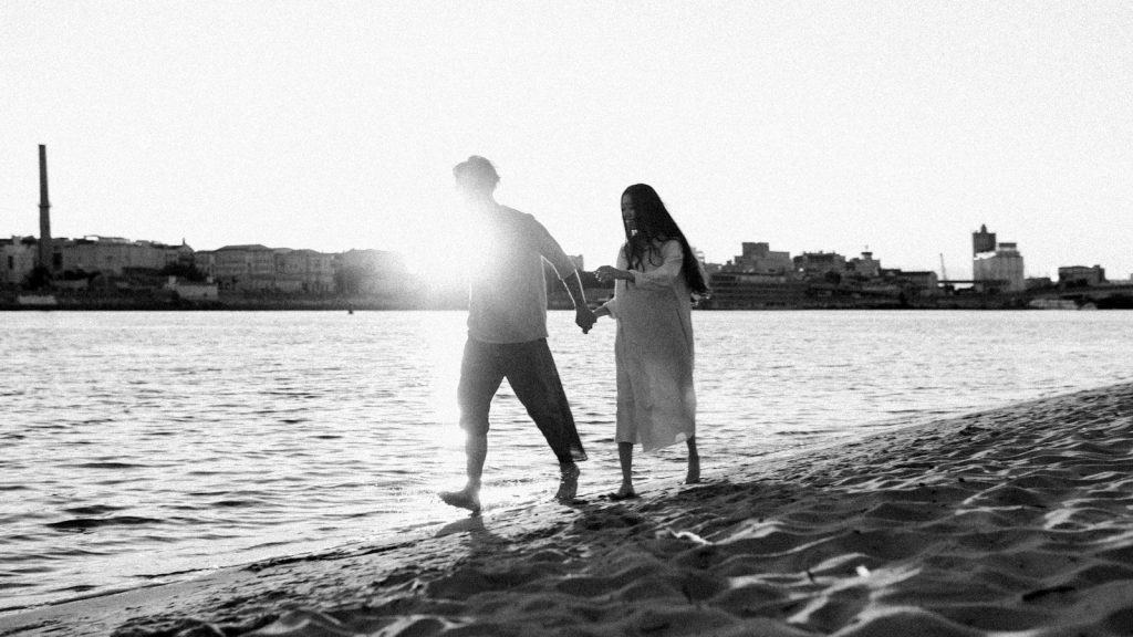 Couple holding hands while walking along a sandy beach at sunset.
