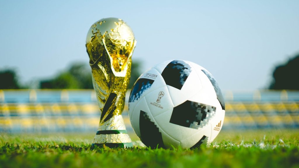 FIFA World Cup trophy beside a soccer ball on a football field.