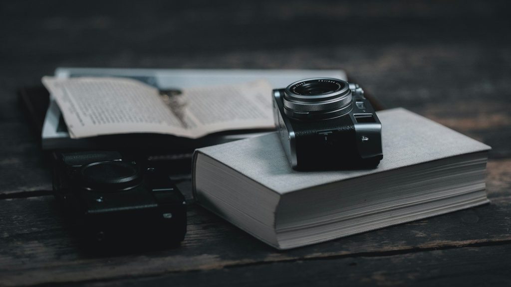 Stack of books with a camera resting on top beside an open book.