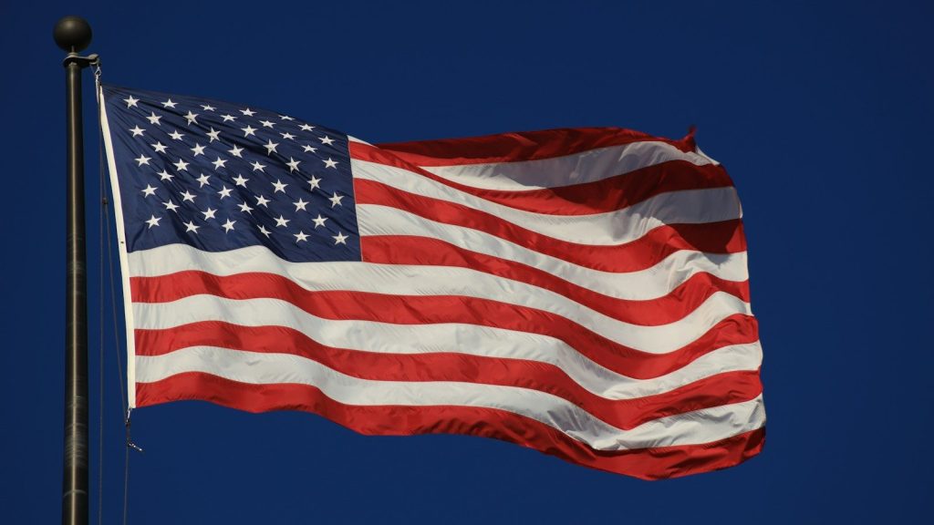 An American flag waves against a clear blue sky.