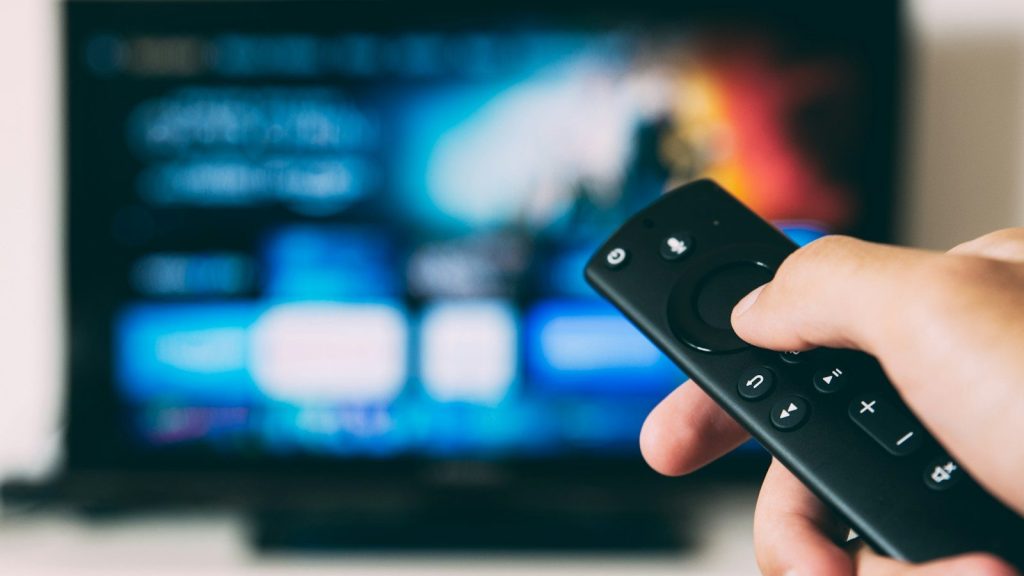A person holding a TV remote pointed at a television.