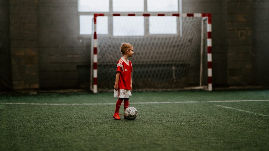 boy standing beside a soccer ball near a soccer net.