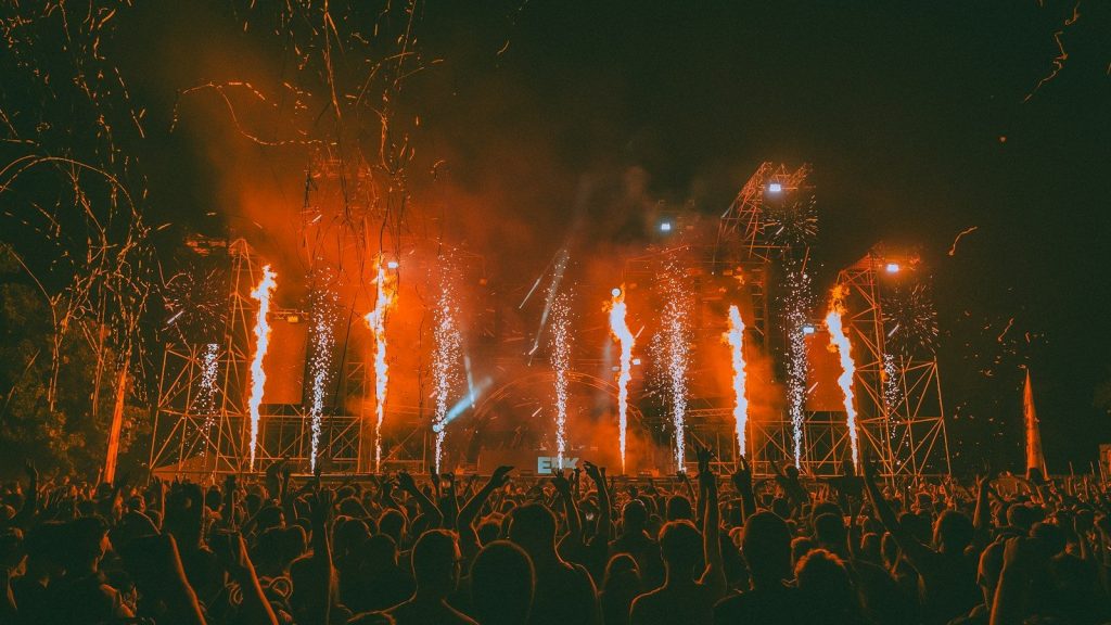 Fireworks erupt over a cheering crowd at a concert.