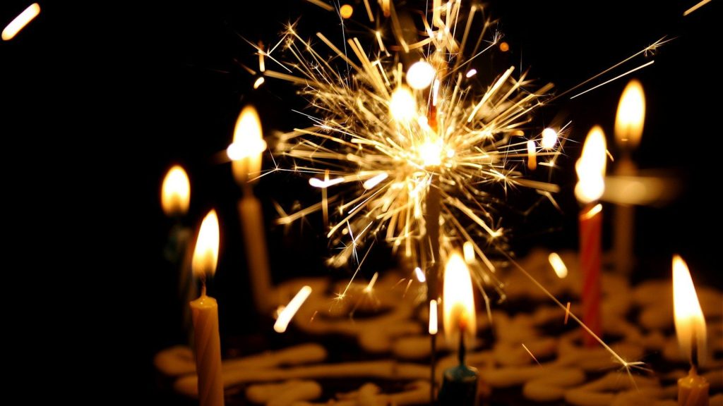 Birthday cake with lit candles and sparkling fireworks in the background.