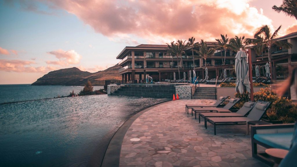 Luxury beachfront resort with an infinity pool, palm trees, and ocean views at sunset.