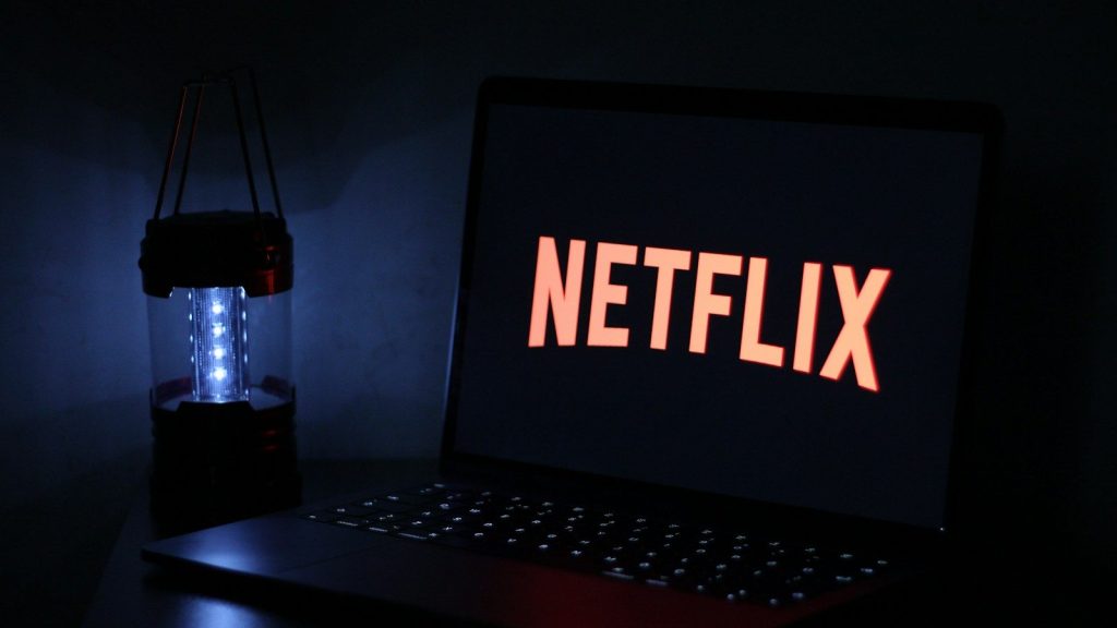 Laptop displaying the Netflix logo in a dark room beside a lantern