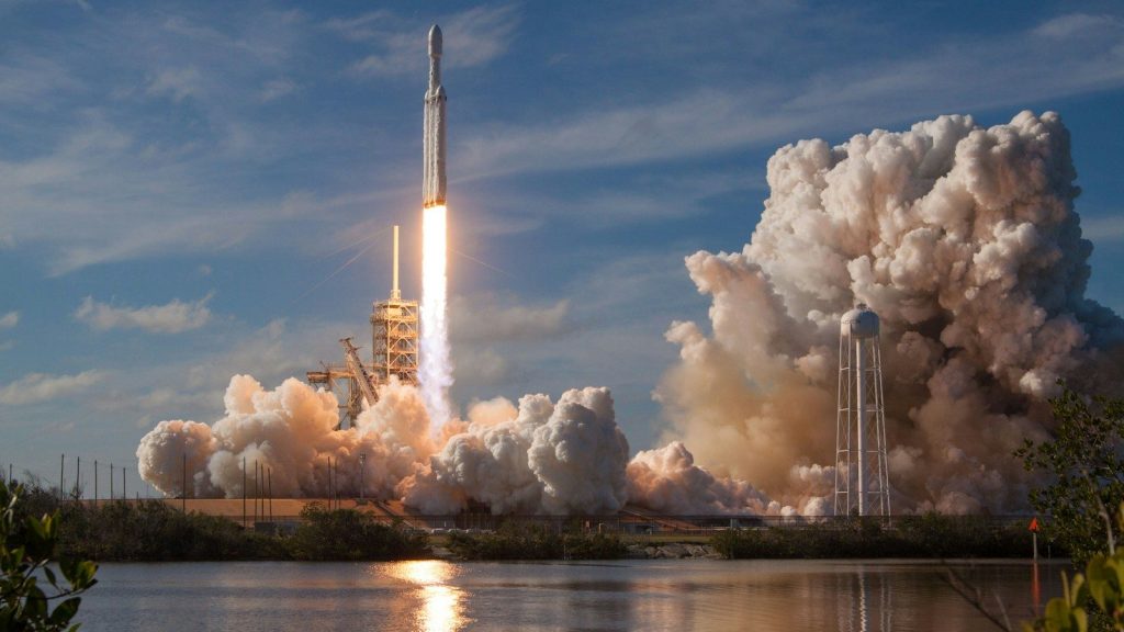A commercial rocket launches into a clear sky above the launch site.