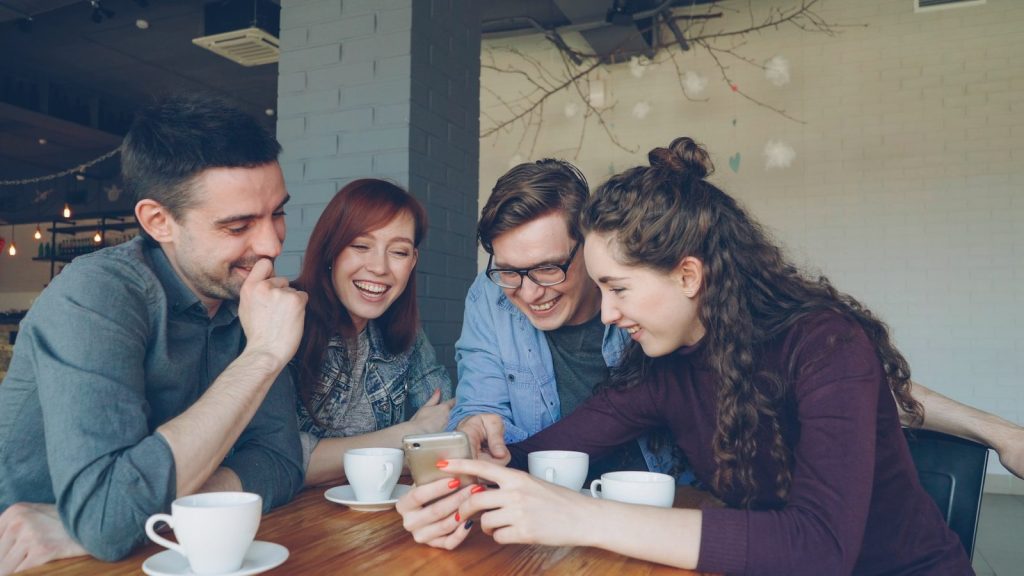 Friends smile while looking at a smartphone together, reacting to online content.
