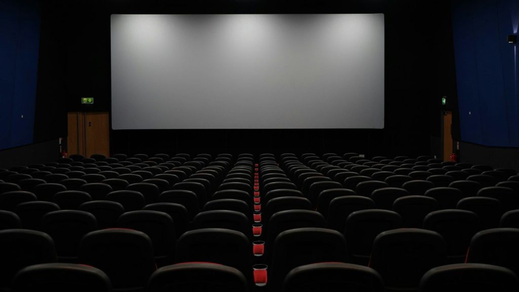 Empty movie theater with rows of vacant seats facing a large projection screen.